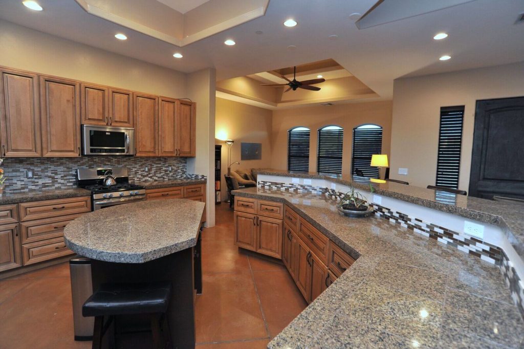 Kitchen remodel with recessed lighting, woodgrain cabinets, granite counters & large island.