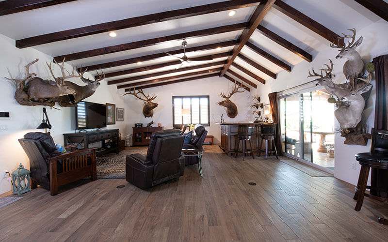 Open-concept living room with exposed beams and recessed lighting on ceiling, wood floors, and sliding glass doors on right side.