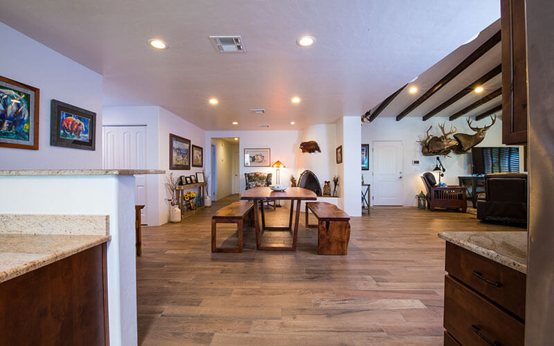 Open-concept whole-home remodel in Tucson, with recessed lighting, dark cabinets and dining table with benches, and exposed beams on ceiling in living area.