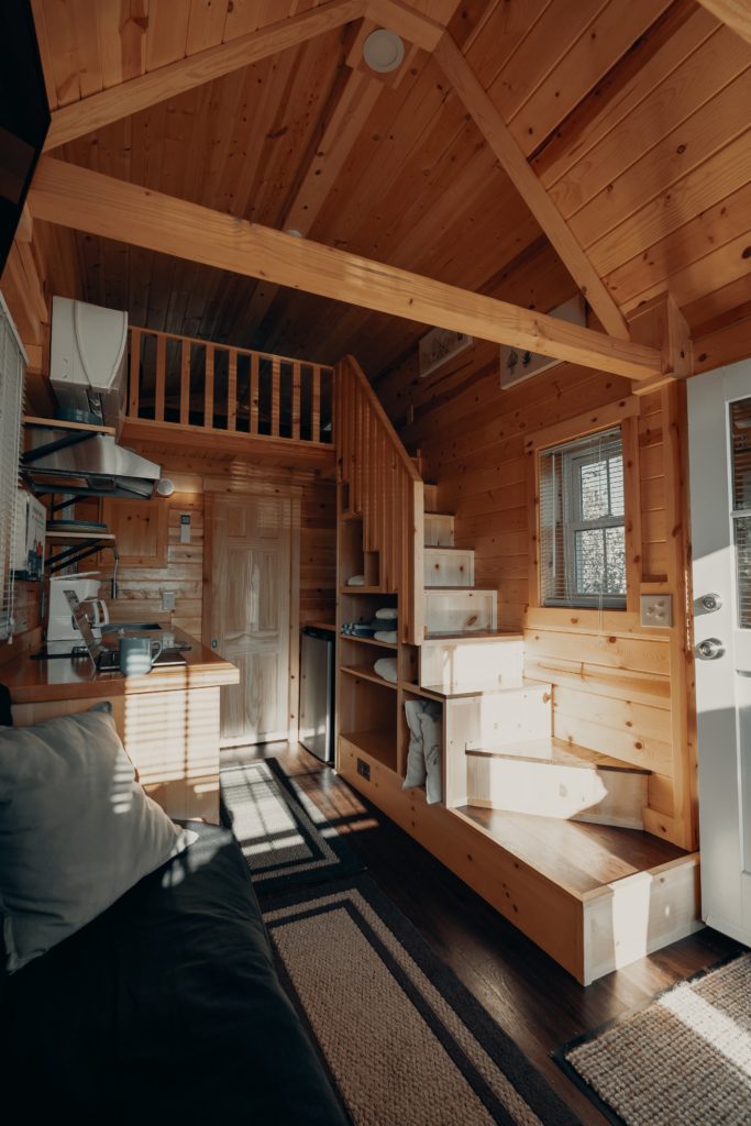 Interior of a two-story "tiny house," or casita. Wood-slat vaulted ceiling, small staircase, rugs on the floor.