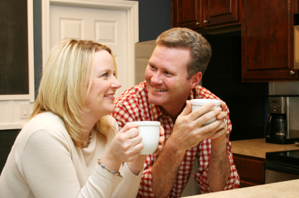 Couple smiling together while holding mugs in an updated kitchen.